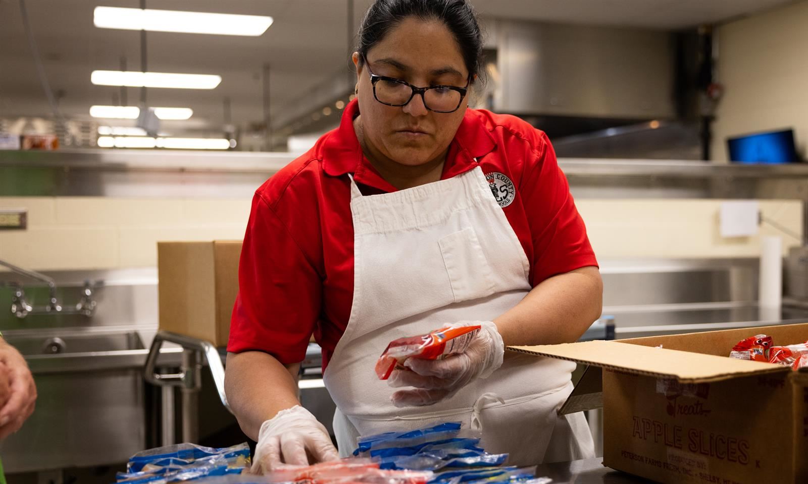 A cafeteria worker replaces packaged apples into a tray
